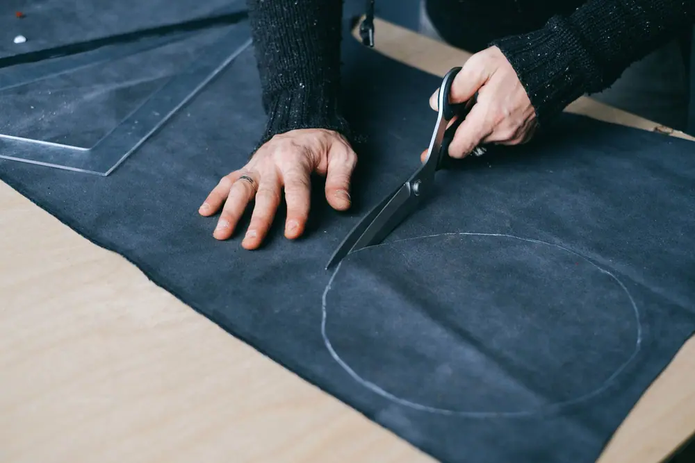 Mains coupant un tissu aux ciseaux sur une table